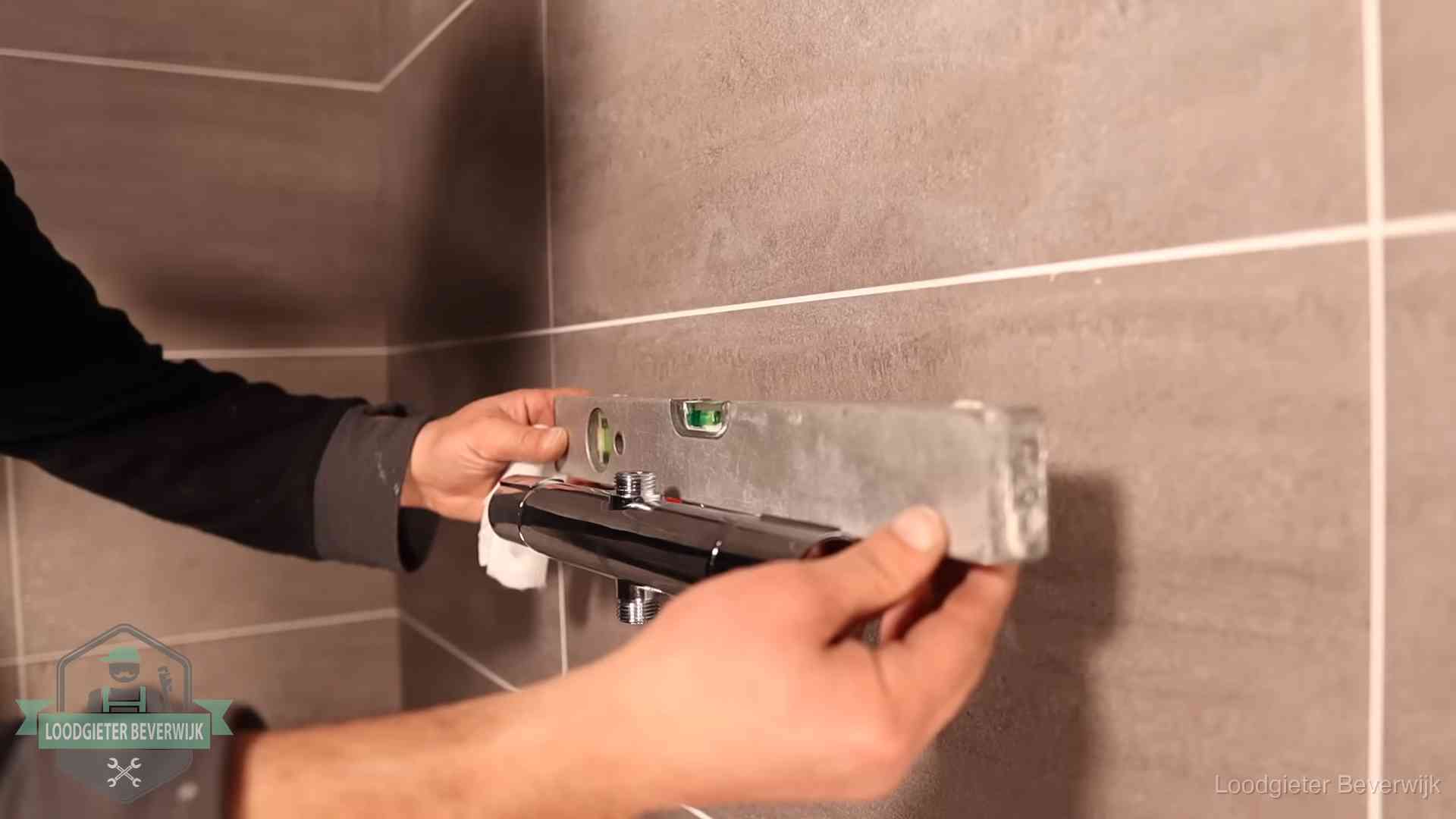 Loodgieter lijnt een douchekraan uit met een waterpas in een woning in Beverwijk