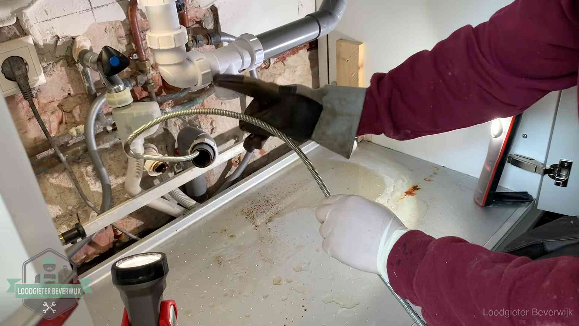 Ontstoppingsveer gaat in een geopende sifonaansluiting onder het aanrecht in Beverwijk