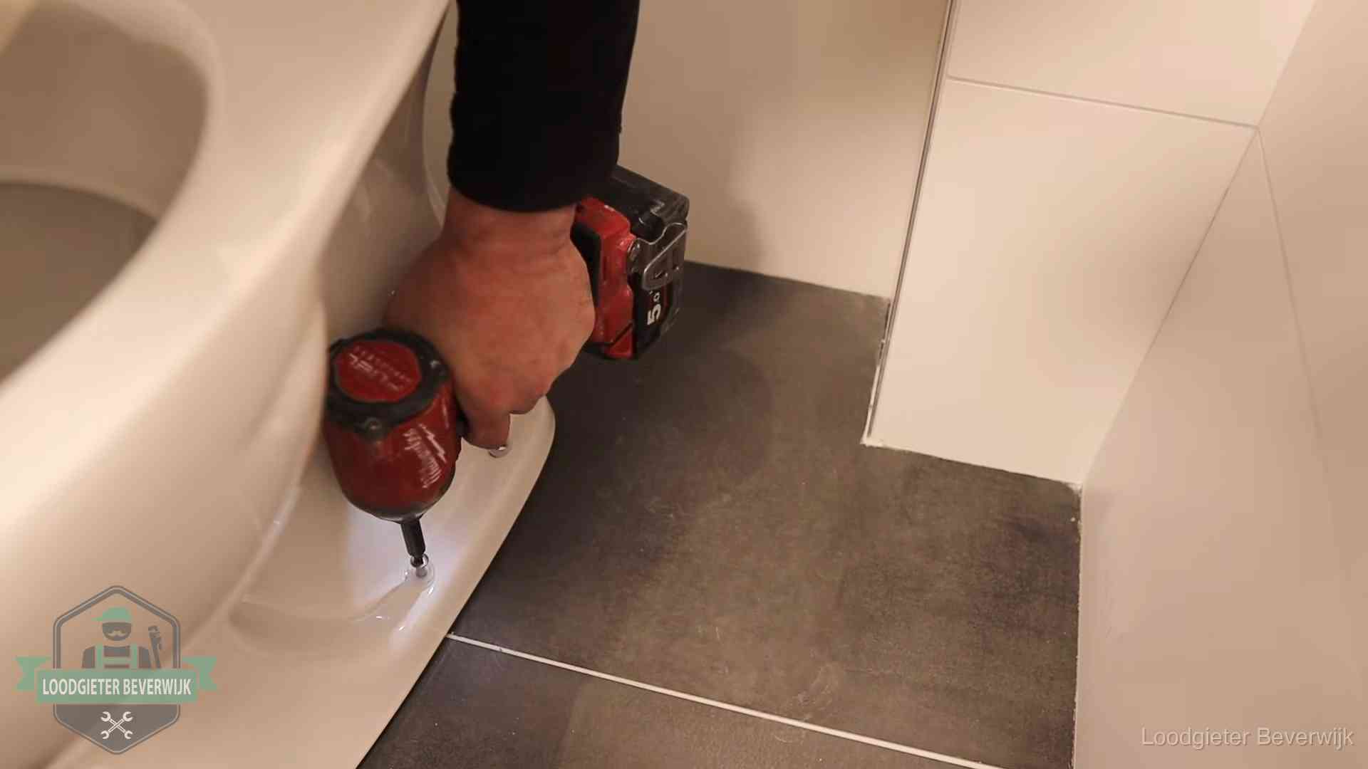Loodgieter zet de voet van een wc-pot vast op de tegelvloer in Beverwijk